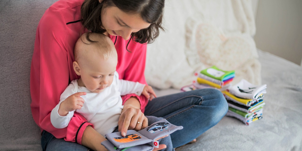 mamma seduta a terra che legge un librino con il suo bambino